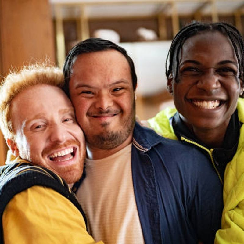 Three diverse friends smiling and hugging, inside a building under construction.