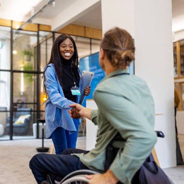 Woman in blue shakes hands with a man in a wheelchair indoors, smiling.