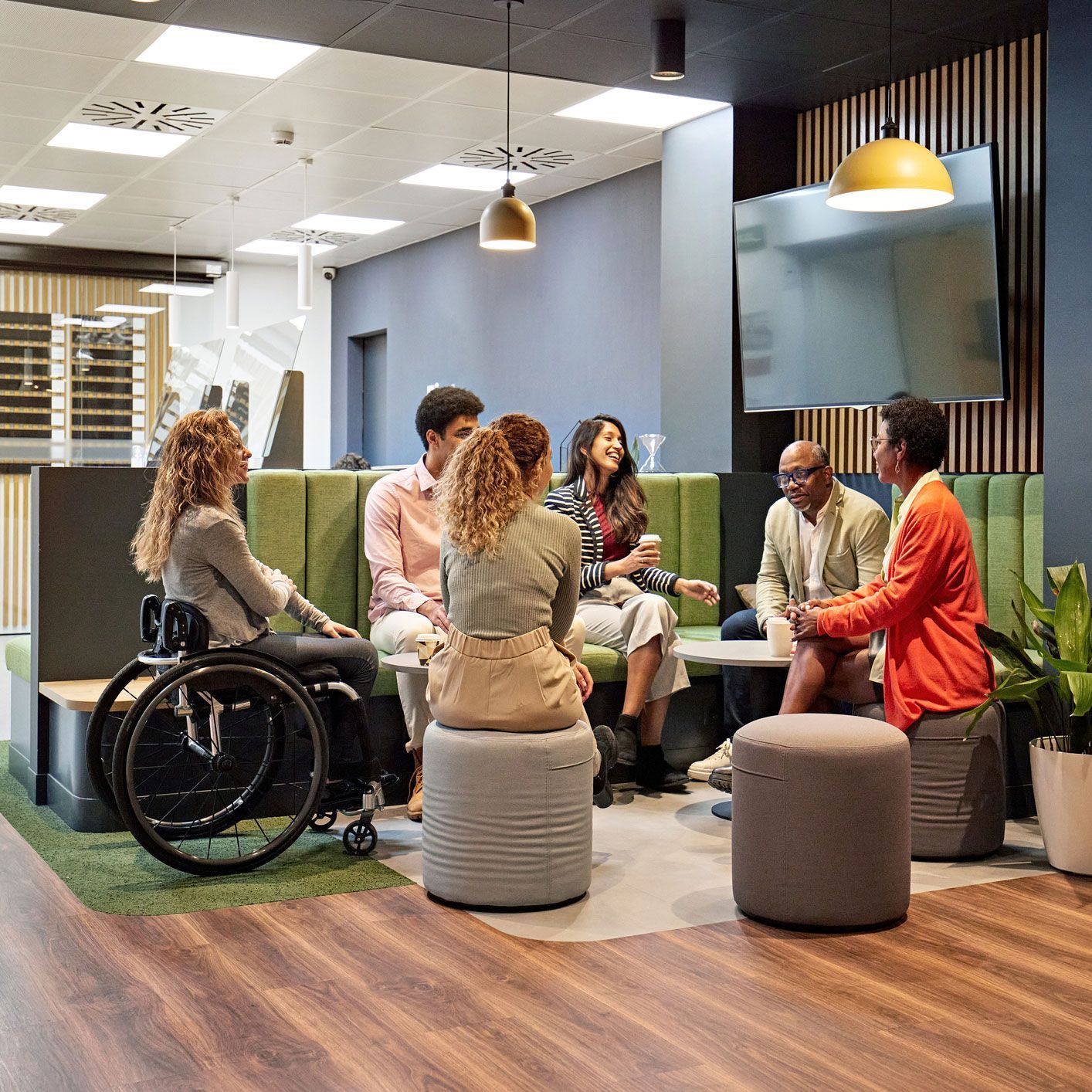 Group of diverse people in a modern office, including a person in a wheelchair, engaged in conversation.
