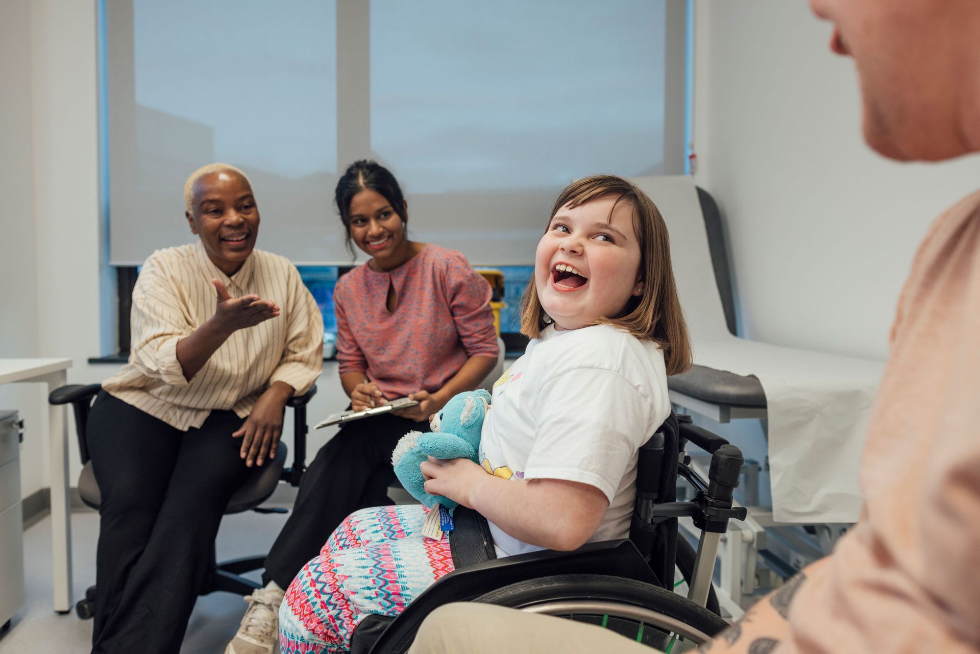 Girl in wheelchair laughs with medical staff and family.