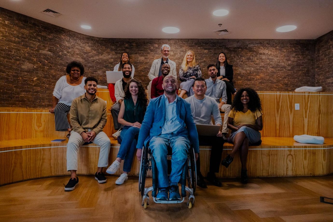 Group of diverse people in a wooden amphitheater, one in a wheelchair, all smiling at the camera.