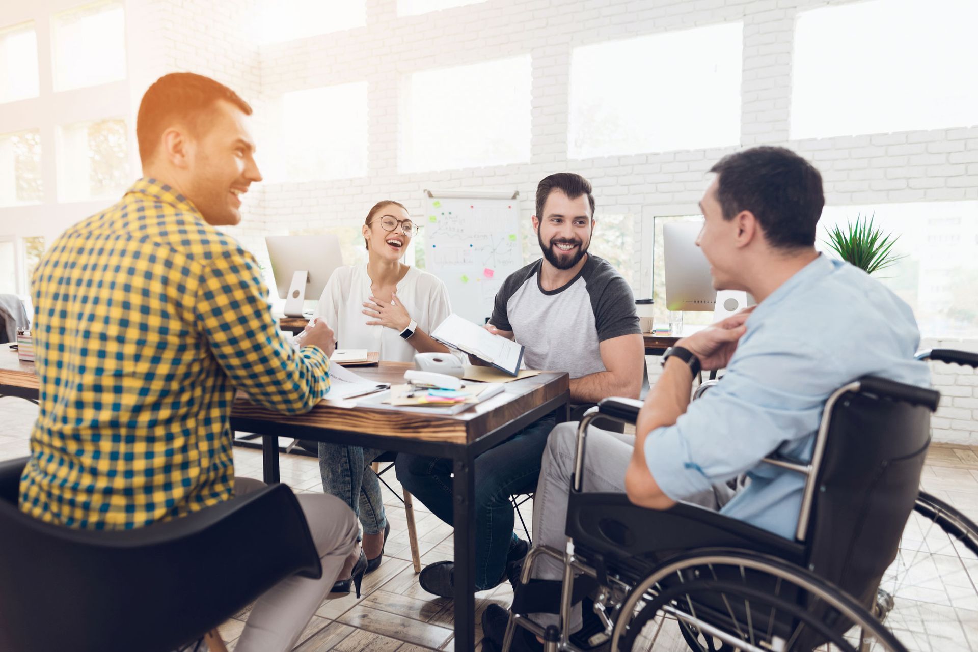 Group of coworkers collaborating around a table; one using a wheelchair. They are smiling and engaged.