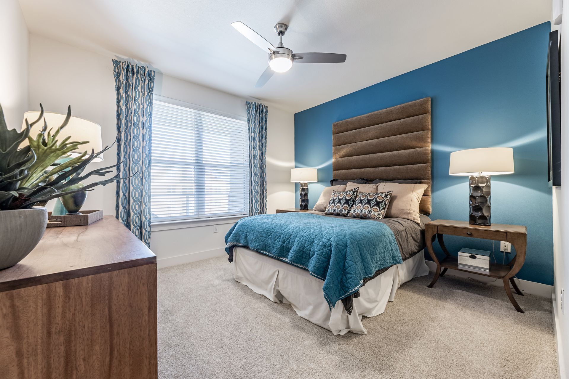 A bedroom with a bed, nightstand, lamps, and a ceiling fan at Parkside at Craig Ranch.