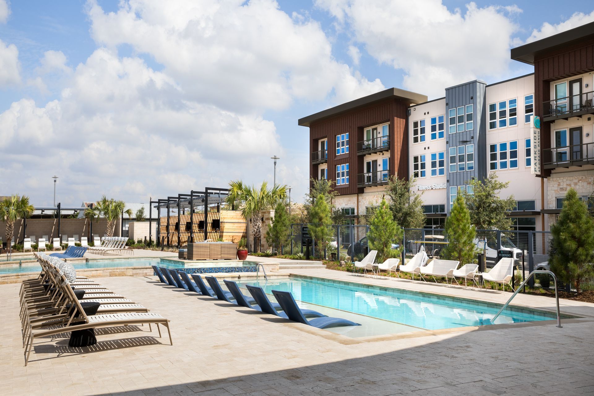 There is a large swimming pool in front of the apartment building at Parkside at Craig Ranch with chairs. 