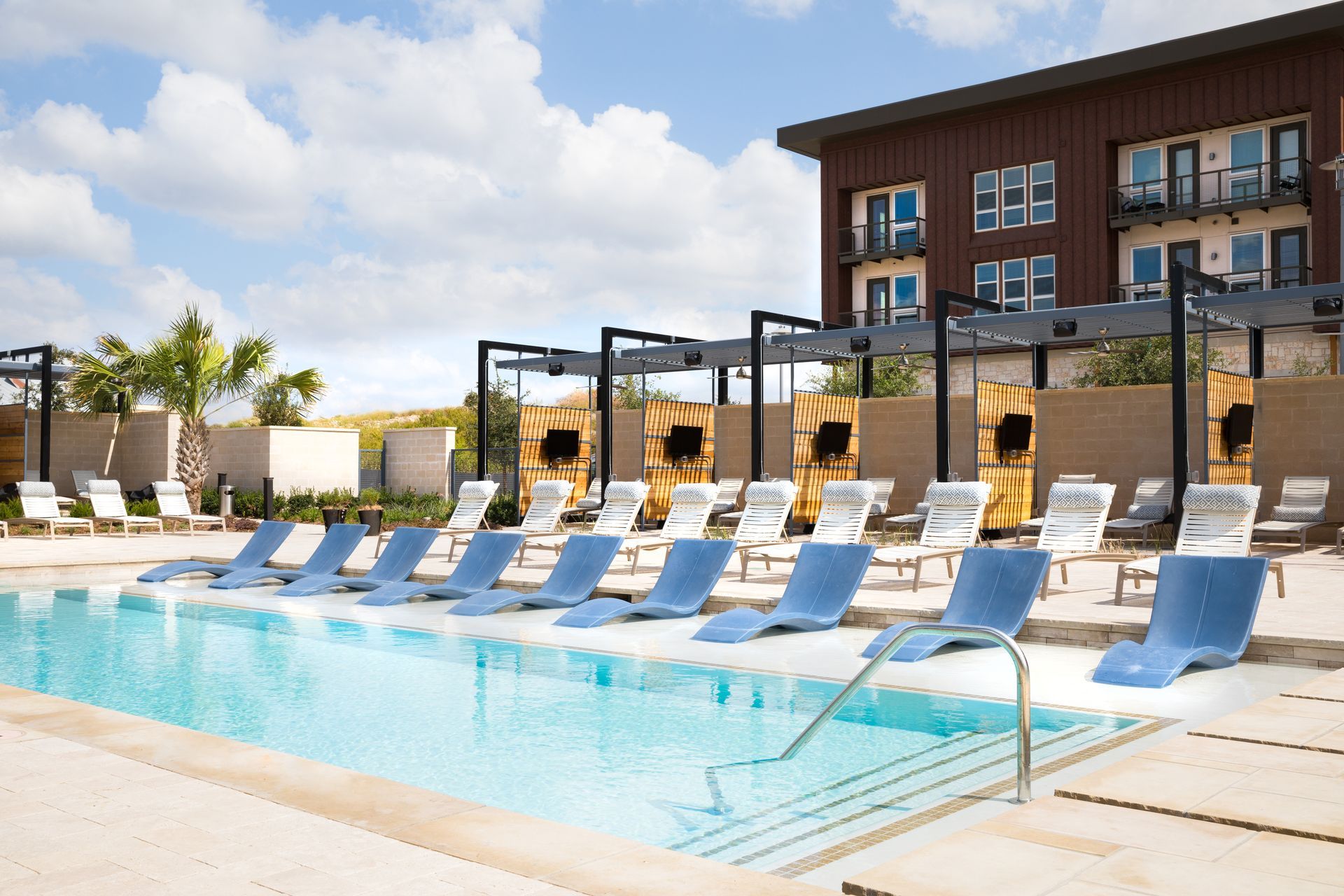 An outdoor swimming pool surrounded by chairs and umbrellas in front of Parkside at Craig Ranch's apartment building.
