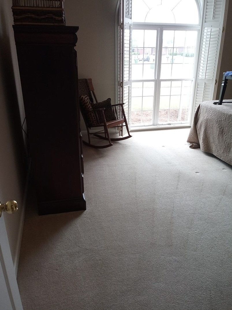 A bedroom with a rocking chair , dresser , bed and window.