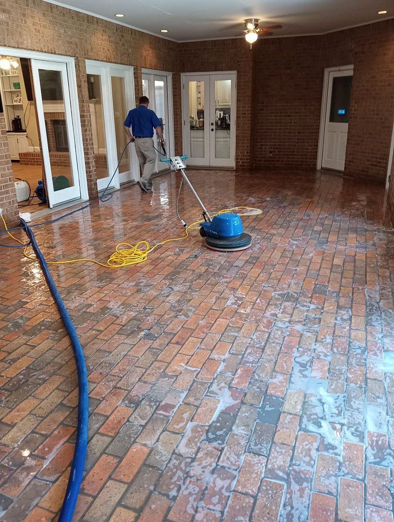 A man is cleaning a brick floor with a vacuum cleaner.