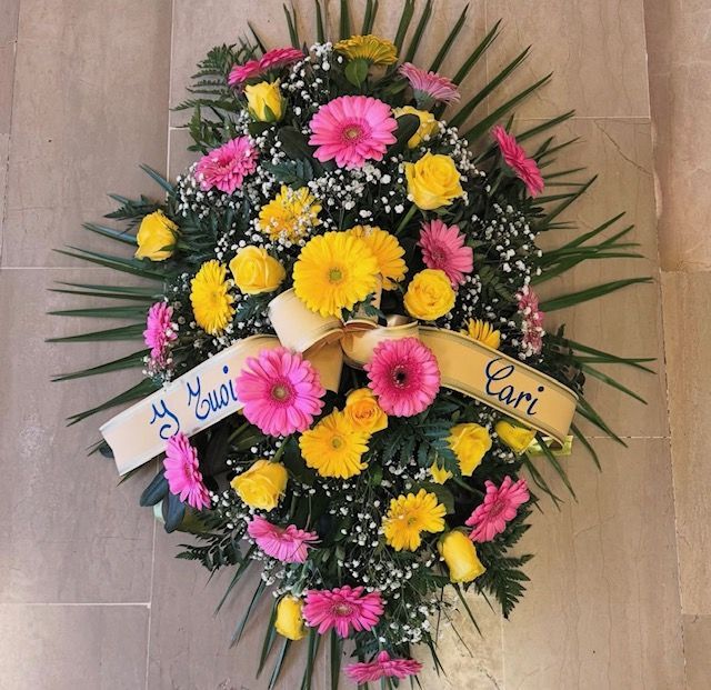 Composizione floreale di fiori gialli e rosa con un nastro con la scritta 