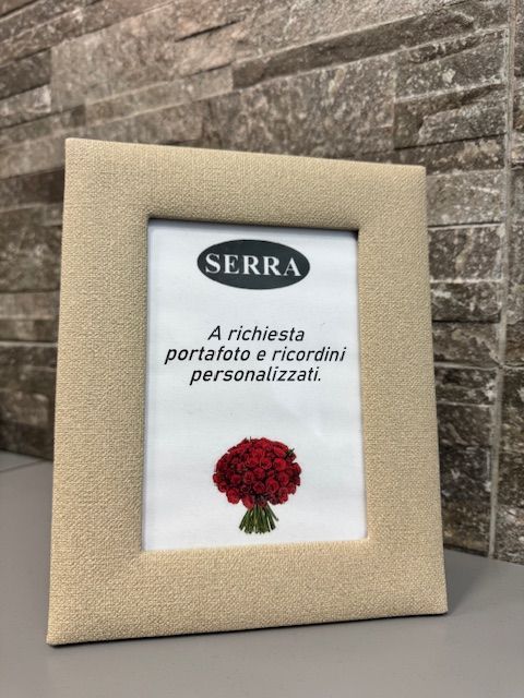 Cornice portafoto in tessuto beige con logo Serra e bouquet di fiori.
