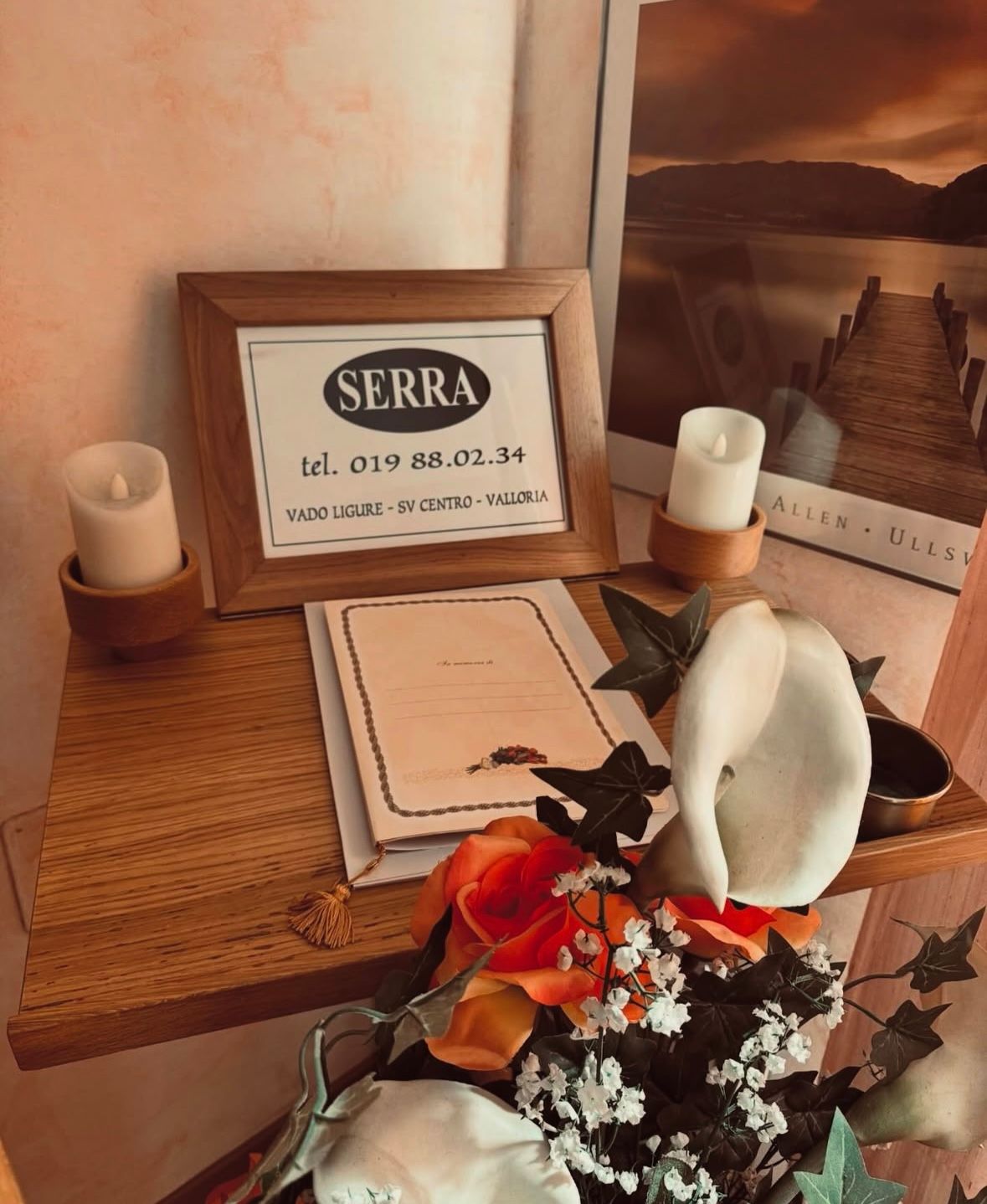 Mensola in legno con insegna incorniciata, candele, fiori e opere d'arte.