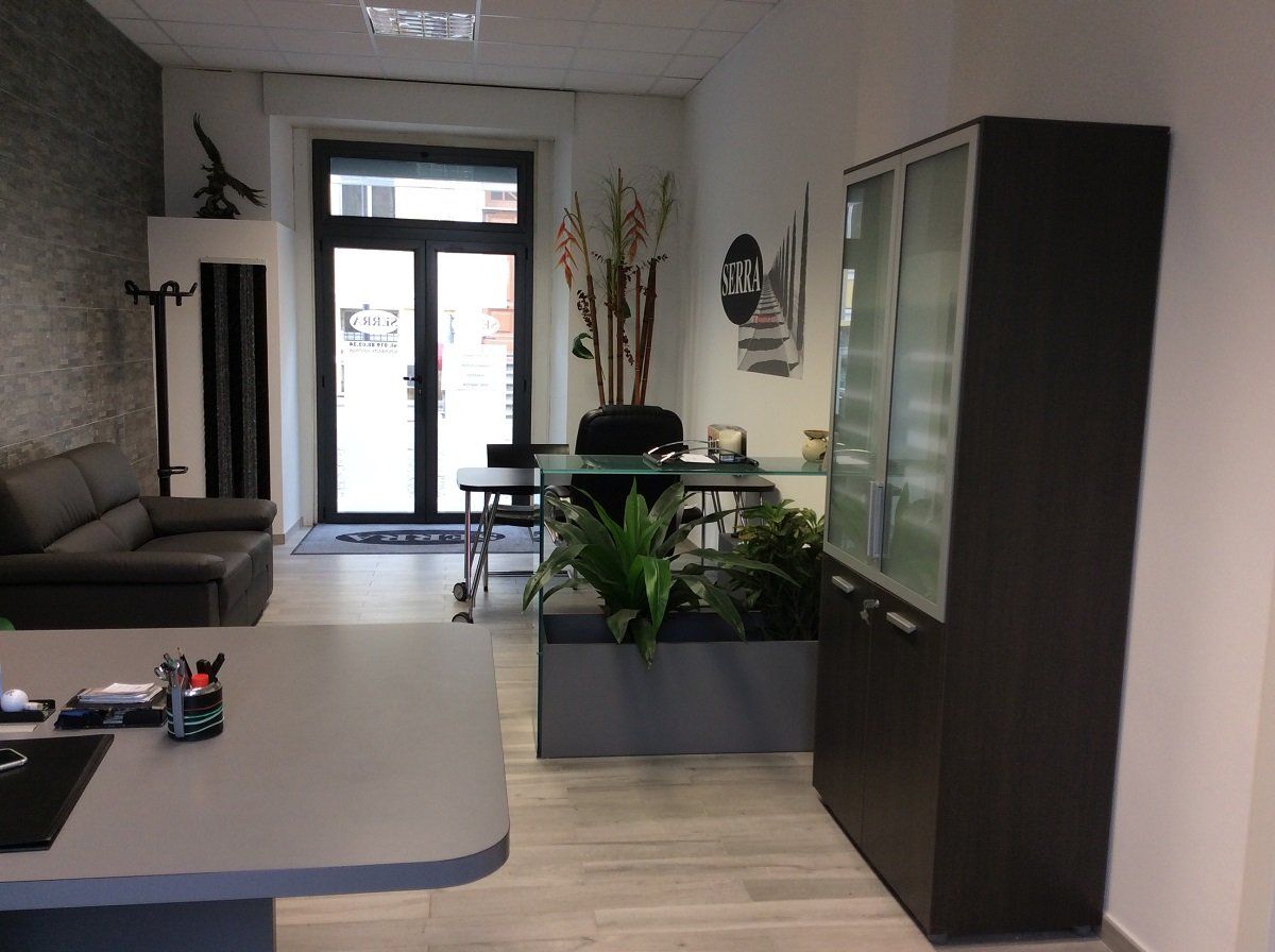 Interno di un ufficio con scrivania grigia, divano, vetrina e porta d'ingresso.