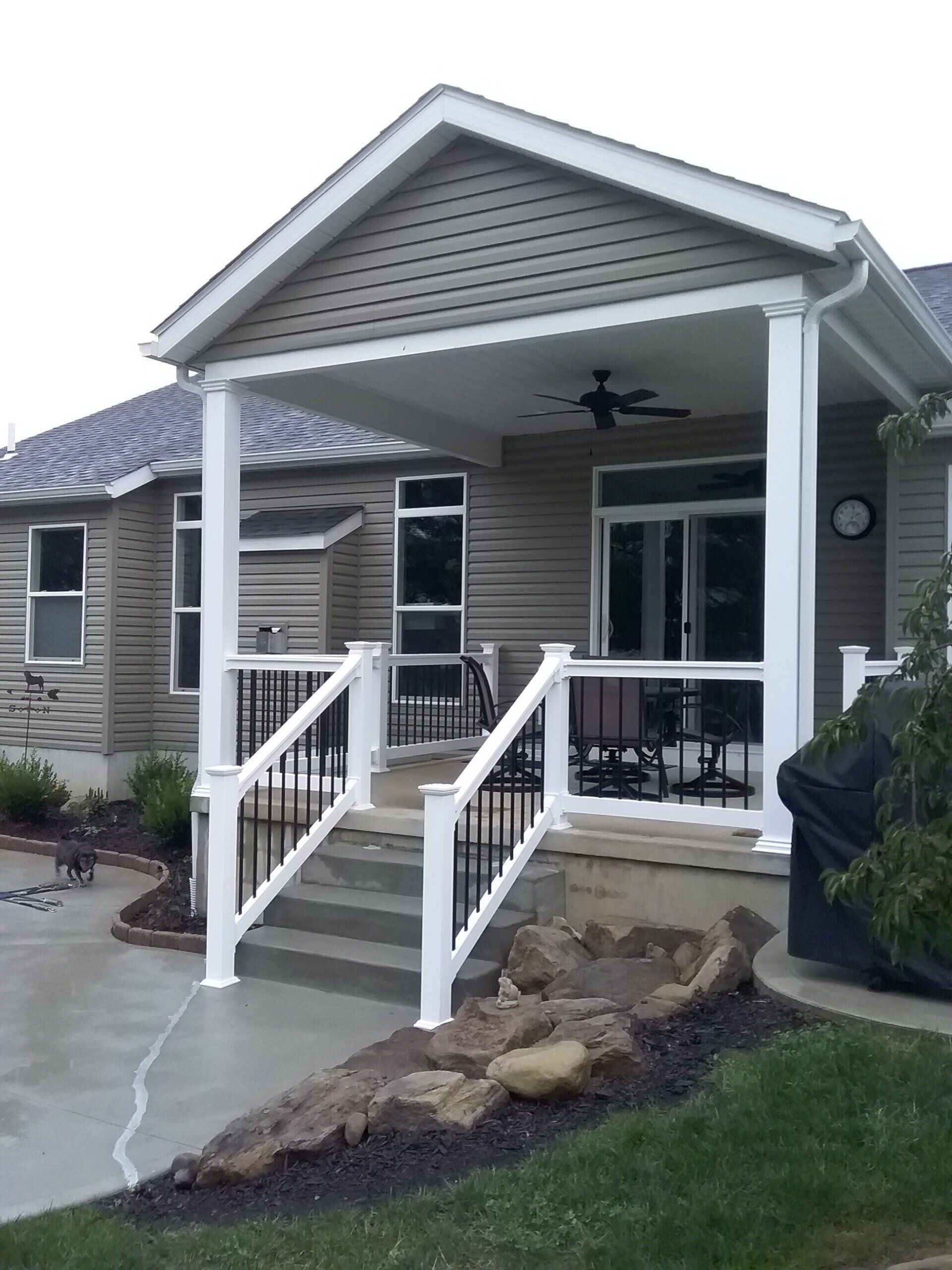 Covered porch with white railings, concrete steps, and a view of a home with a light tan exterior.