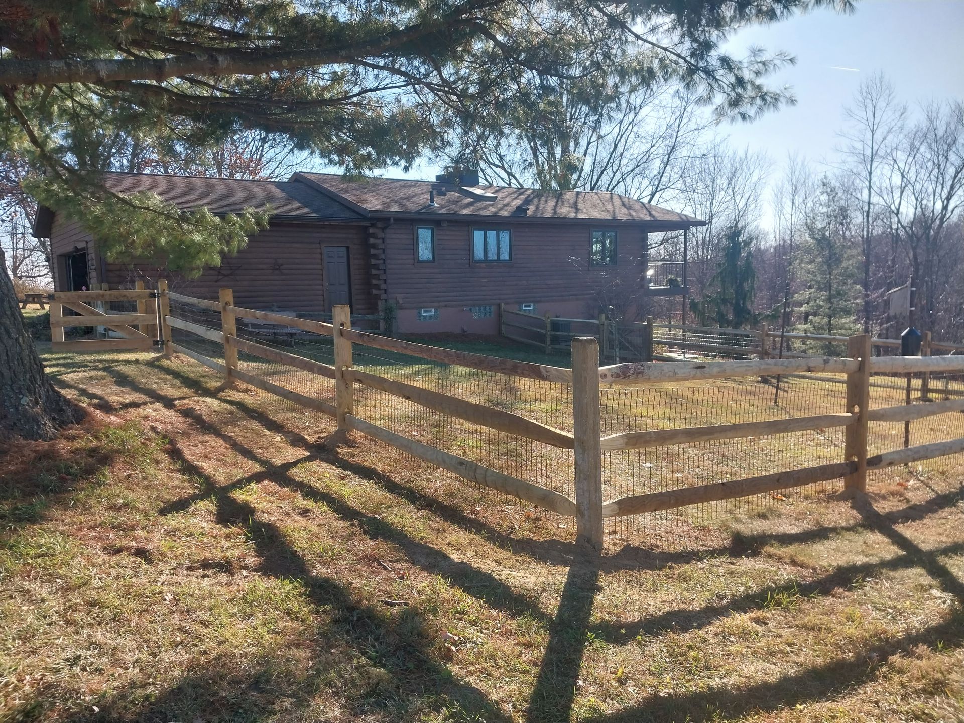 Wooden split-rail fence in front of a brown house on a sunny day.