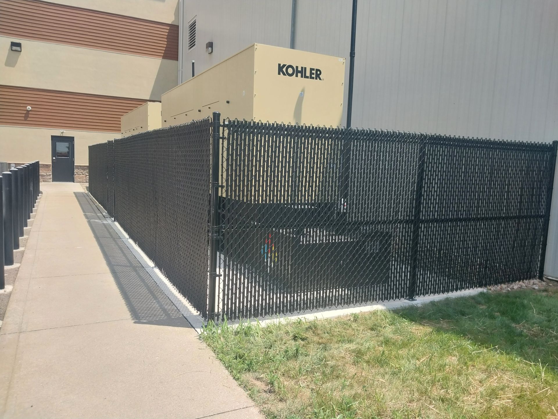 Black fence surrounding an outdoor area with a beige building and a generator that says KOHLER.
