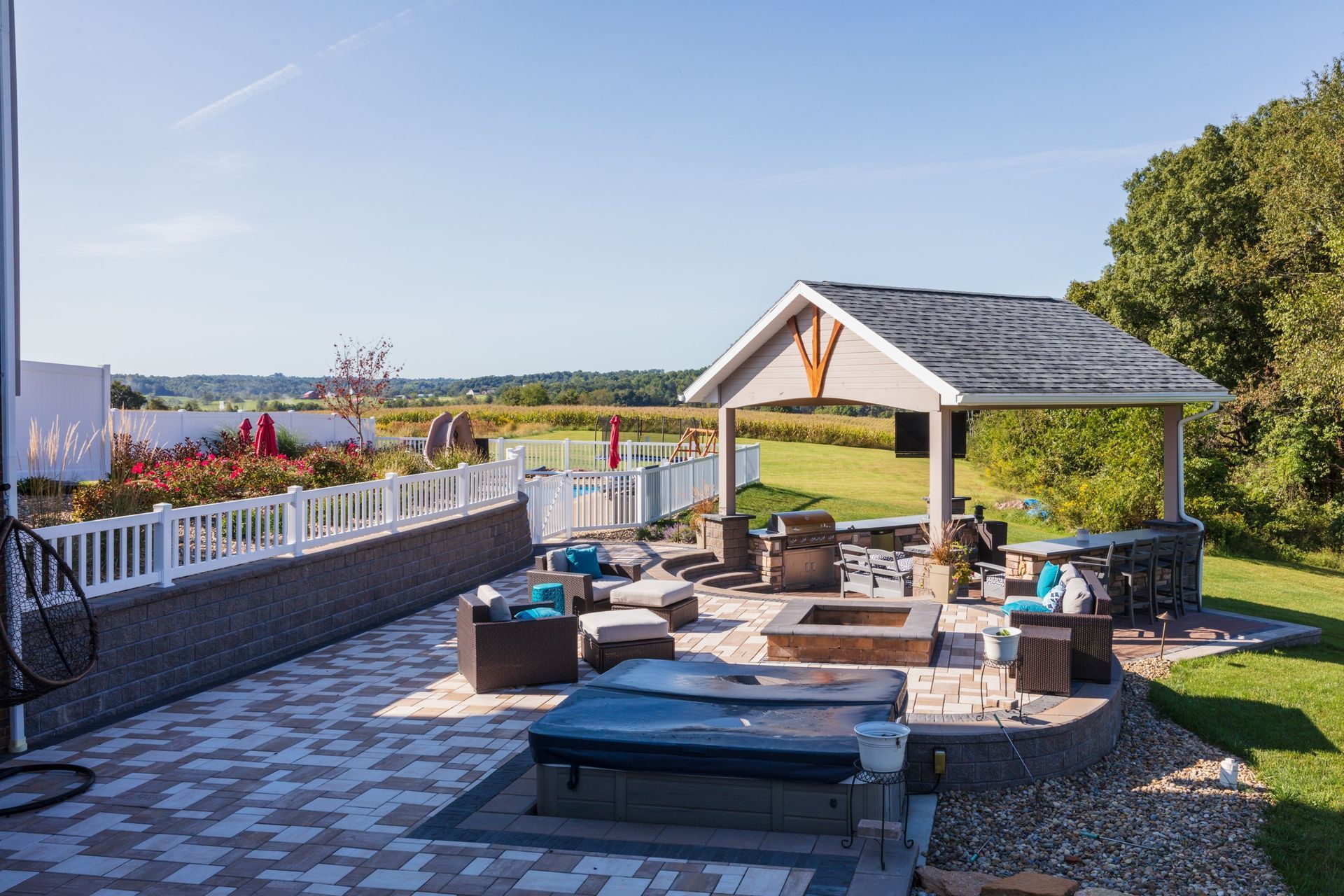 Patio with hot tub, fire pit, and gazebo overlooking a field on a sunny day.