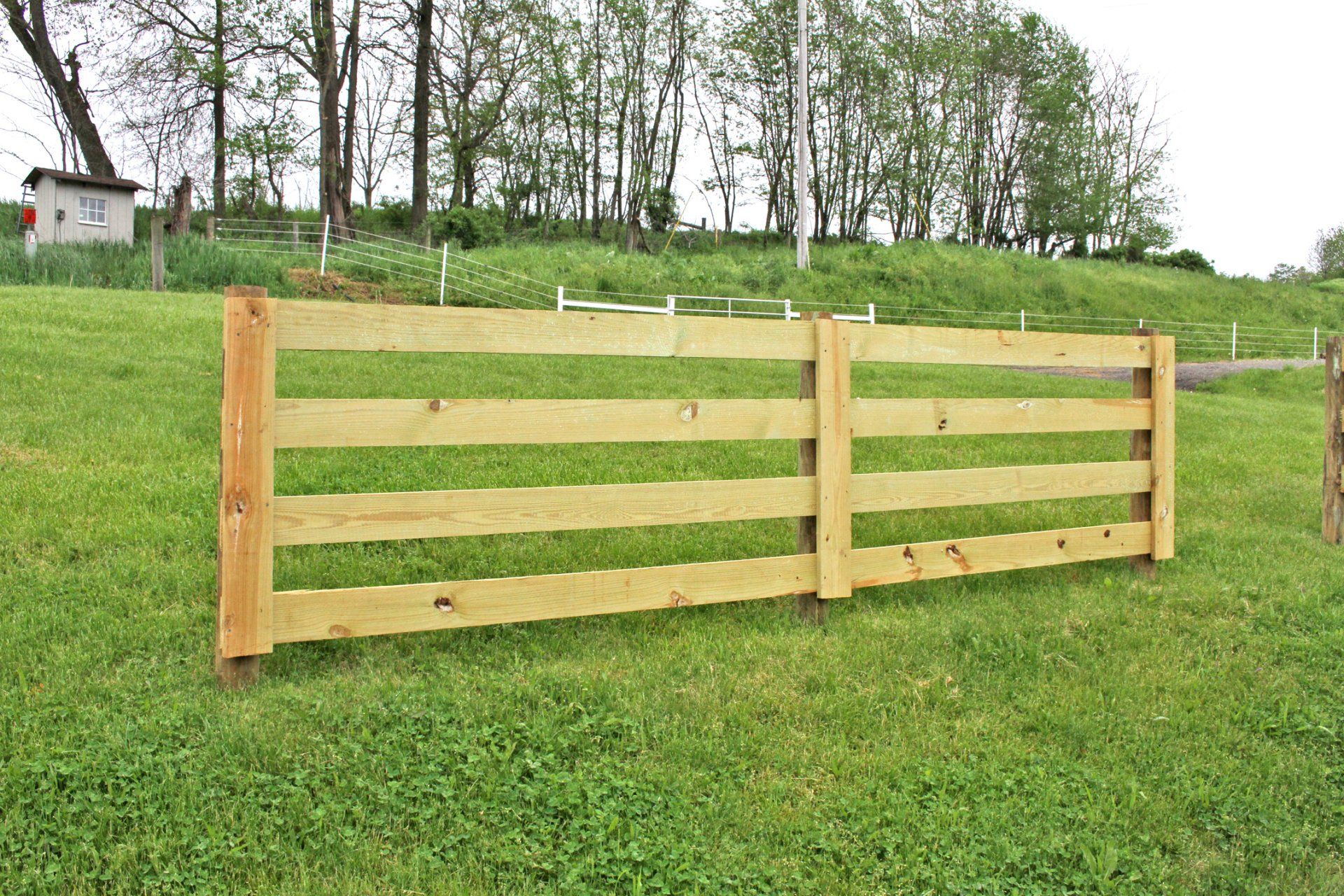 Wooden fence in a grassy field with trees in the background.
