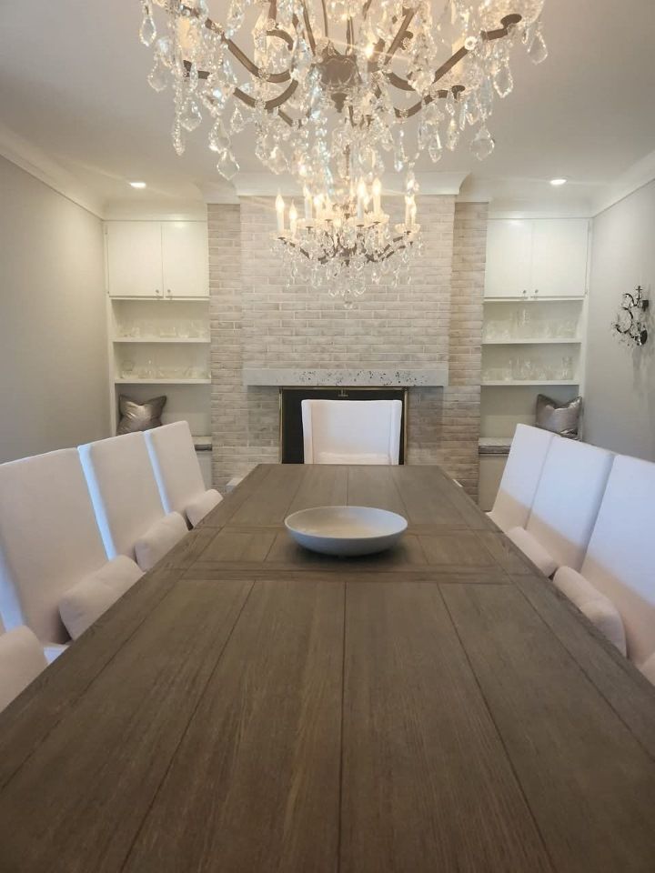 A dining room with a long table and chairs and a chandelier painted white brick
