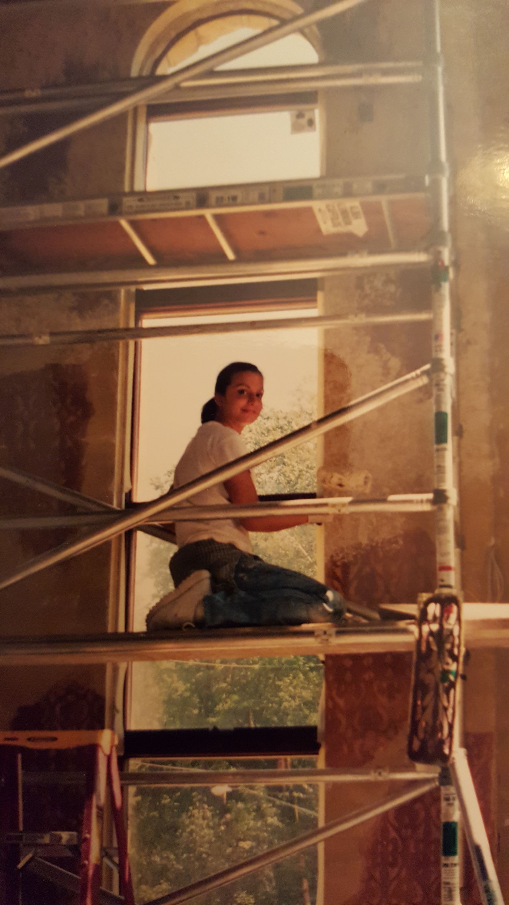 A woman is kneeling on a scaffolding in front of a window.