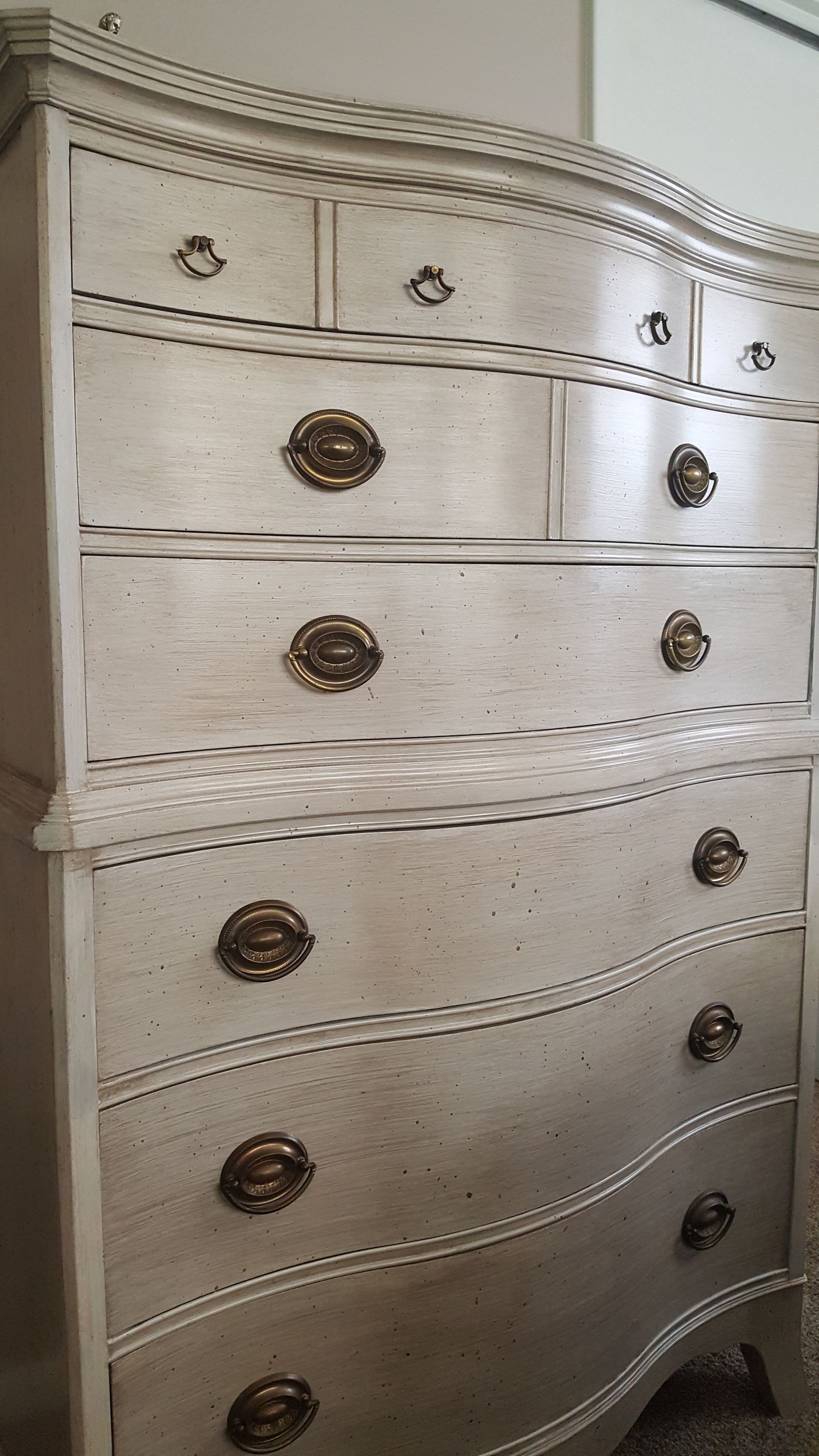 A white dresser with gold handles is sitting in a room.