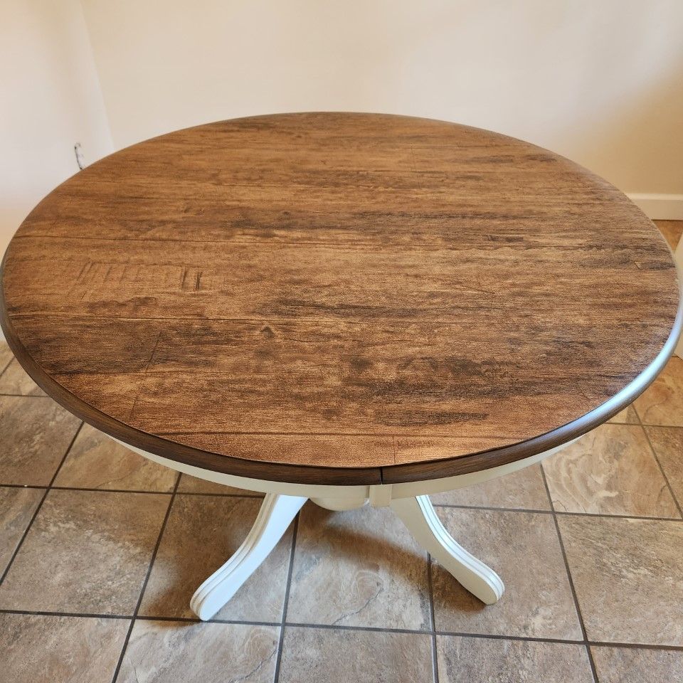 A round wooden table with a white base is sitting on a tiled floor.