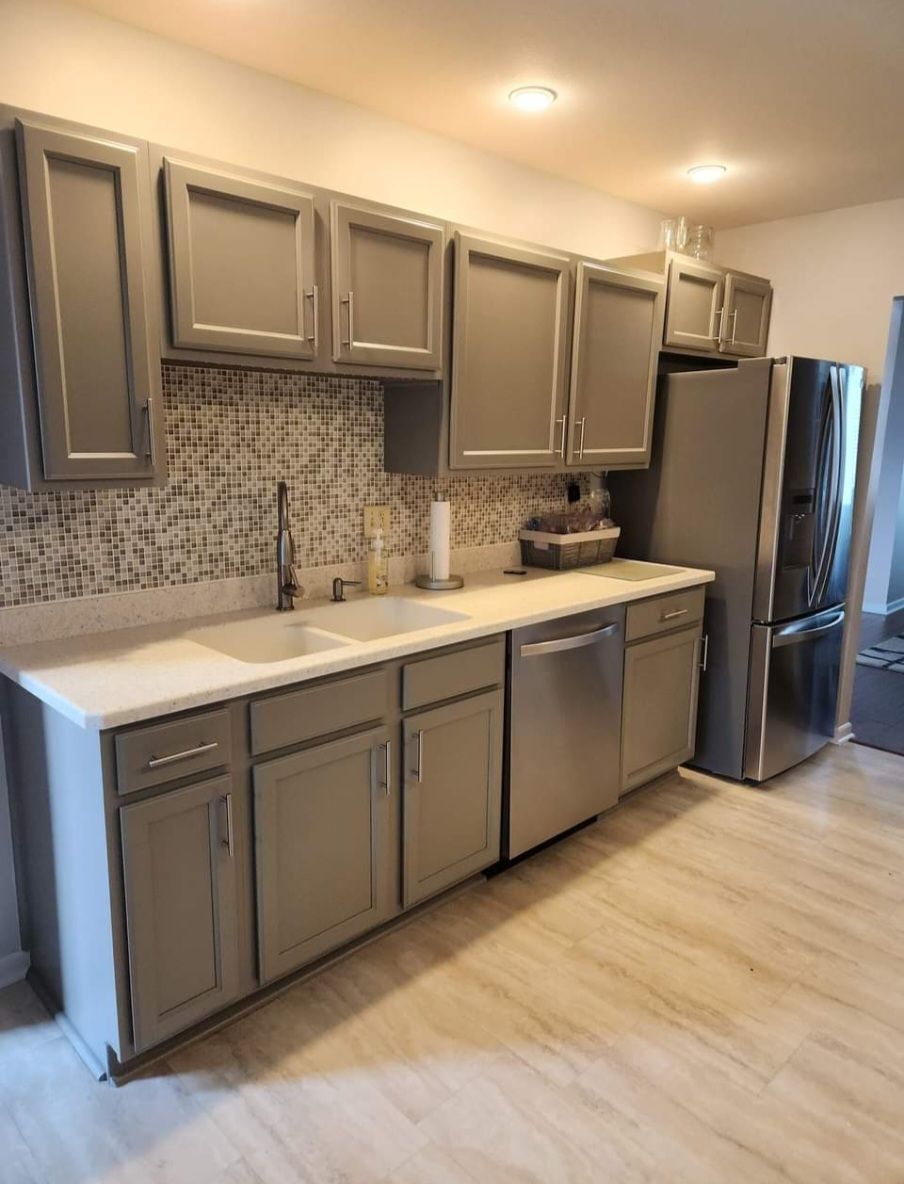 A kitchen with gray cabinets , stainless steel appliances , a sink , and a refrigerator.