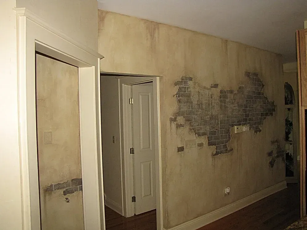 A hallway with a brick wall and a door leading to a room.