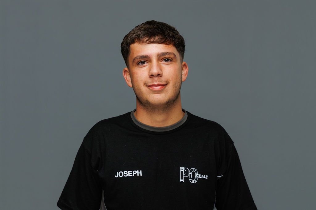 Person in a black T-shirt against a plain gray background, facing forward with a slight smile.