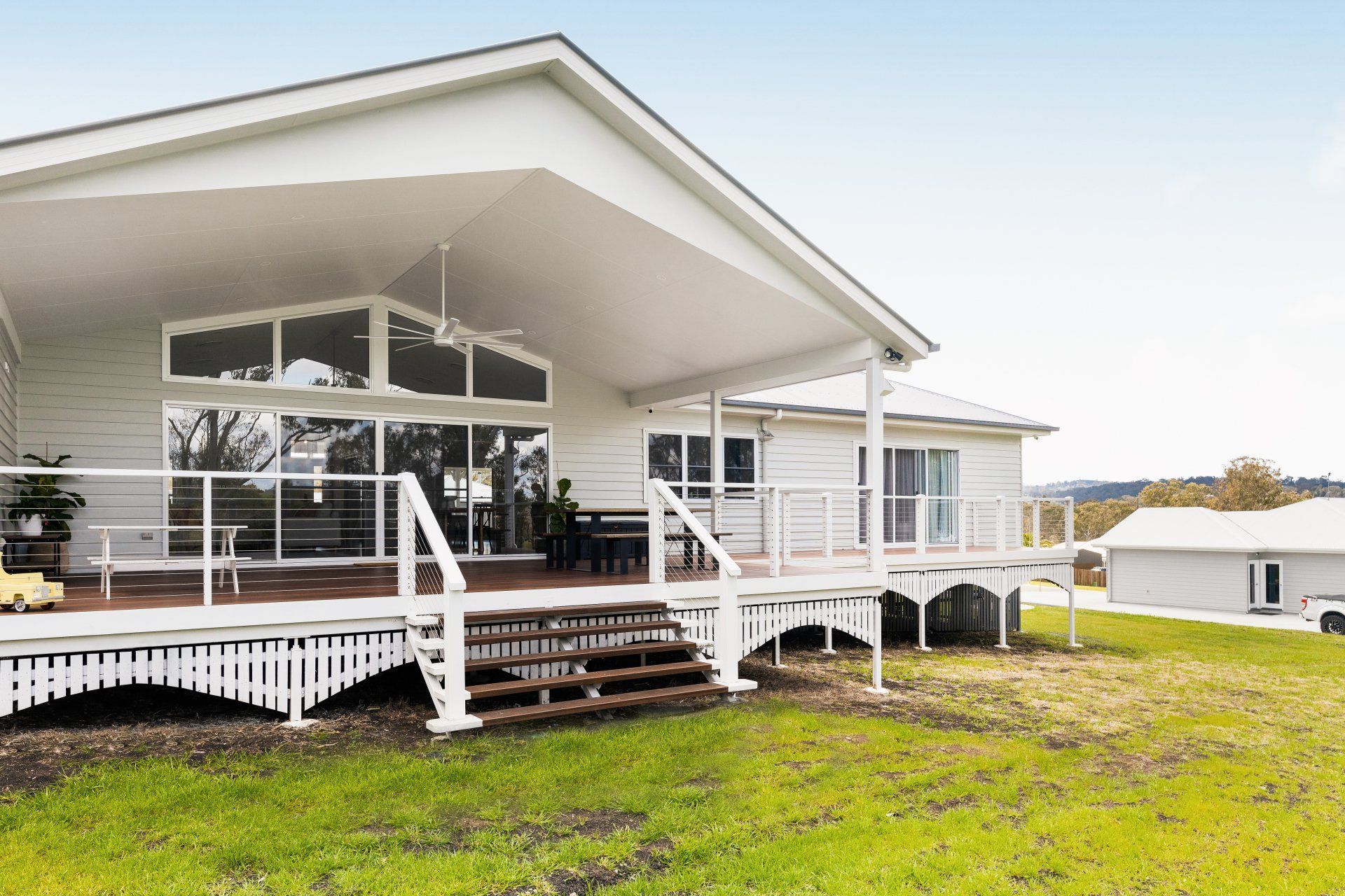 White house with a large deck and covered porch on a grassy hill, overlooking a rural landscape.
