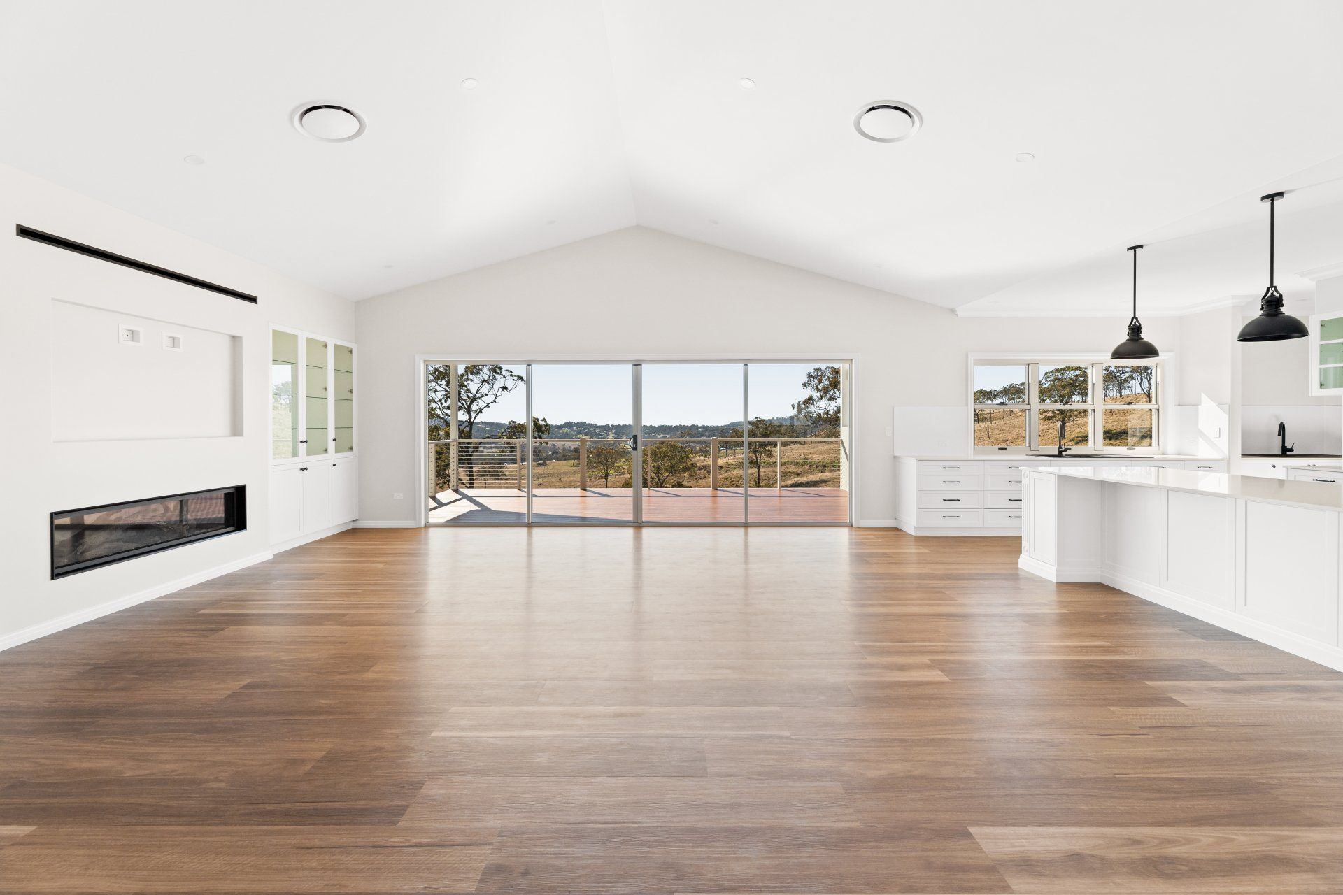Spacious white interior with hardwood floors, large windows overlooking a landscape, and a modern fireplace.