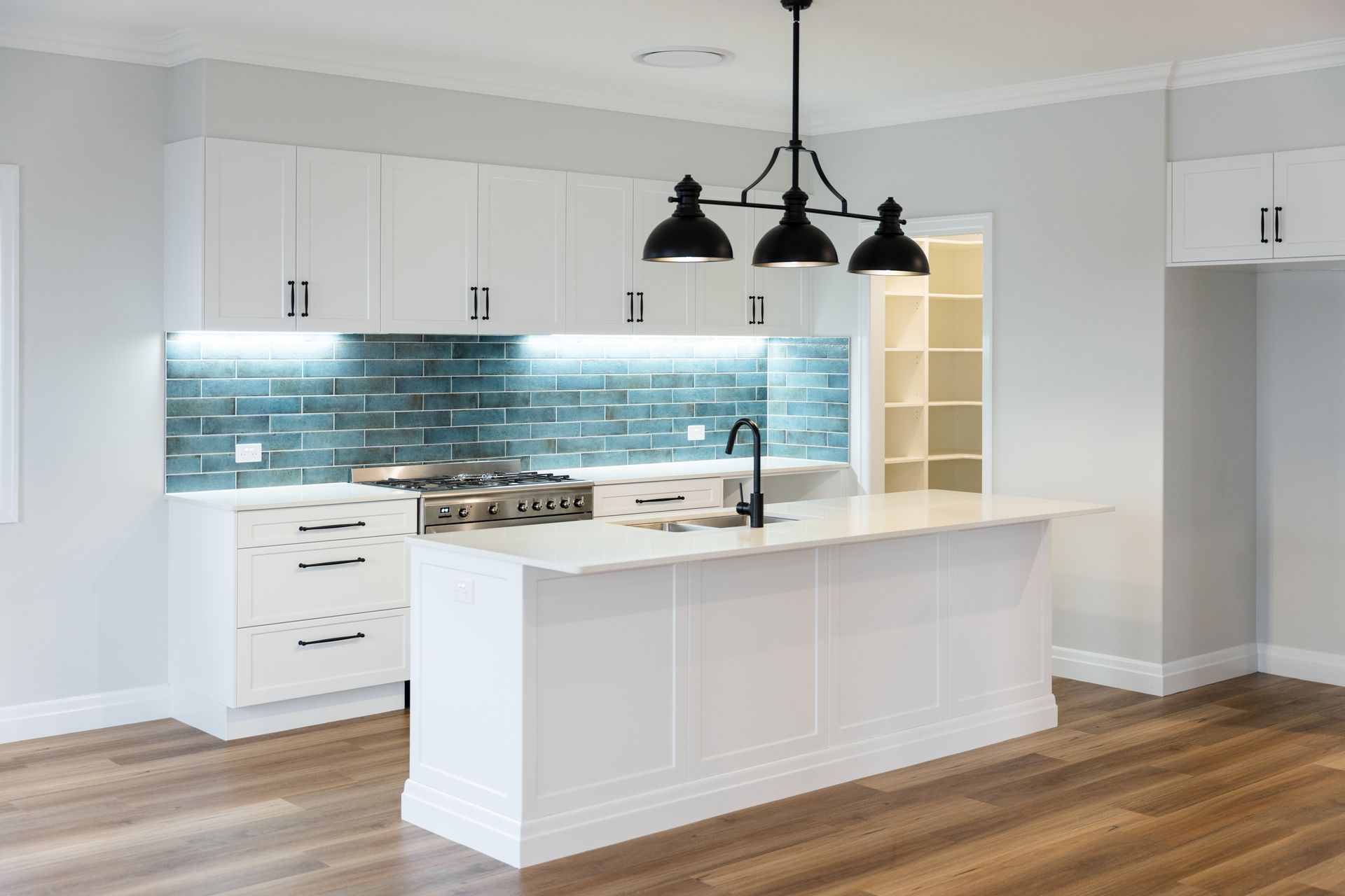 Modern white kitchen with island, blue tile backsplash, and black pendant lights.