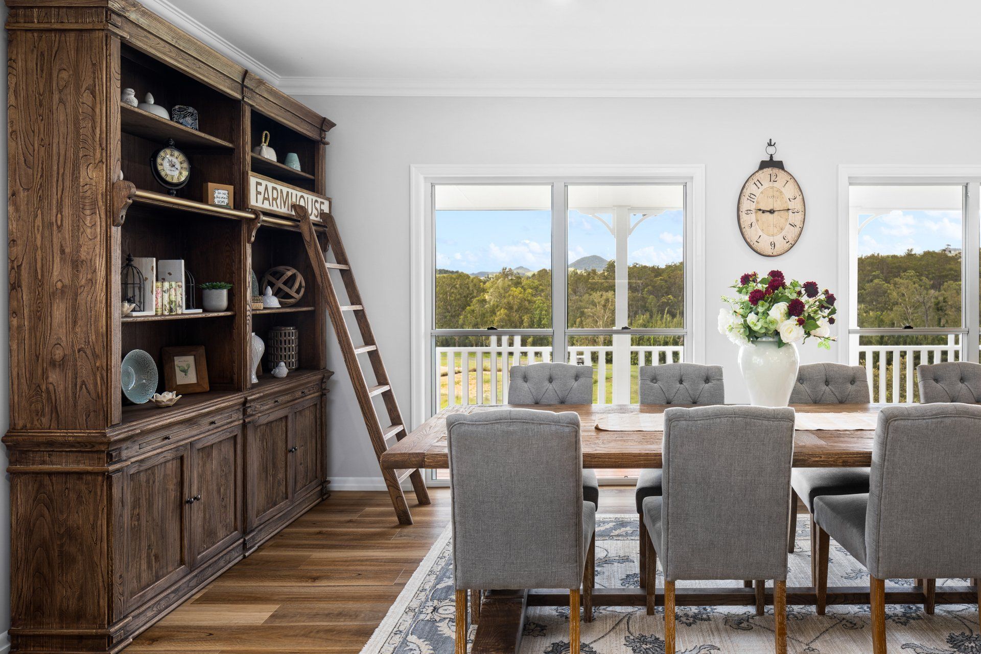 Dining room with wooden bookcase, table, chairs, and large window overlooking a landscape.