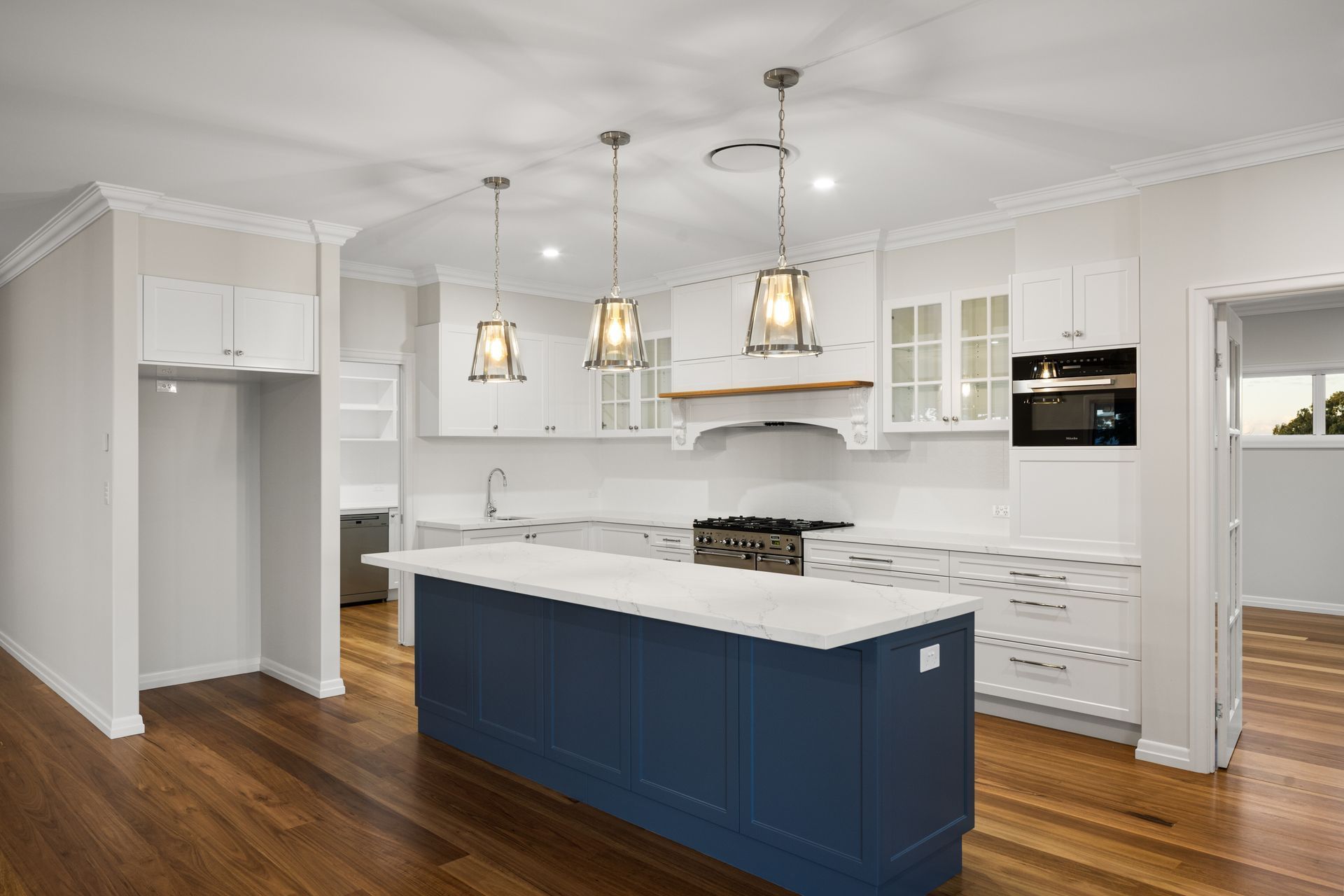 A modern kitchen with a blue island and white cabinets, wood floors, and pendant lights.