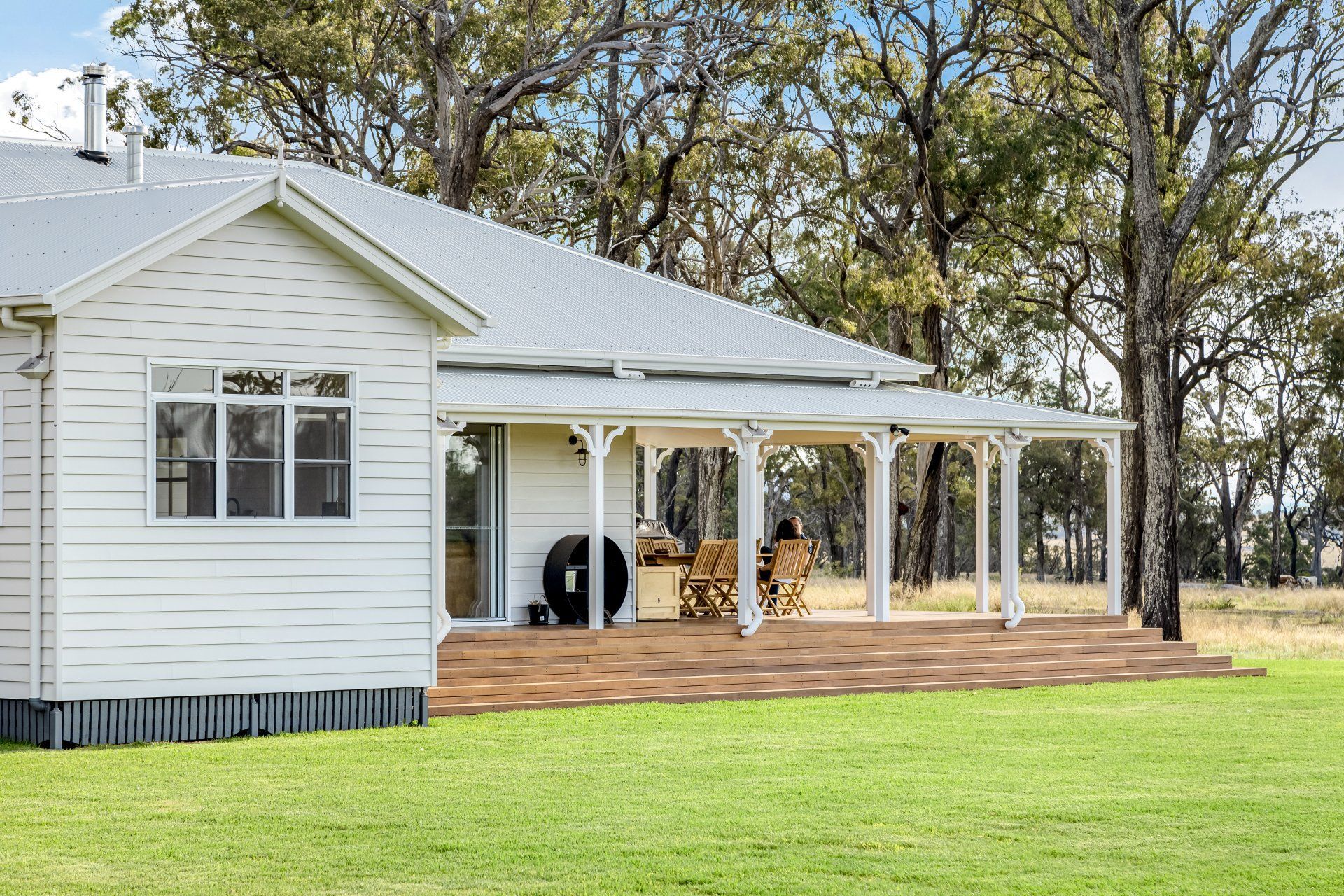 White farmhouse with a long, covered porch on a grassy lawn.