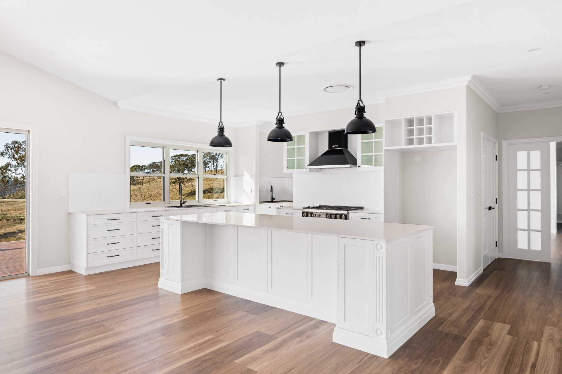 White kitchen with island, black pendant lights, and hardwood floors.