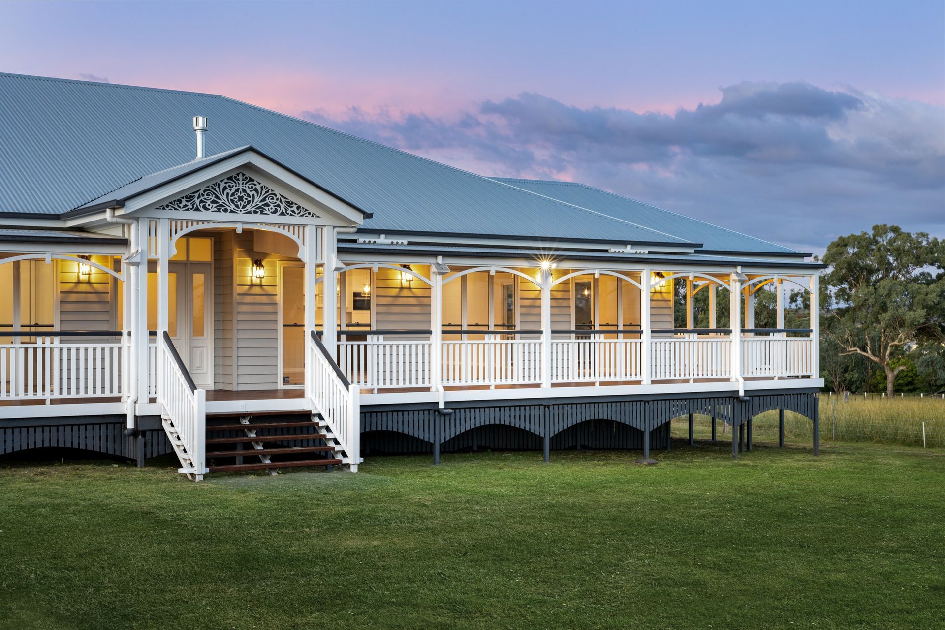 White and gray house with a wide veranda, steps, and a green lawn under a twilight sky.