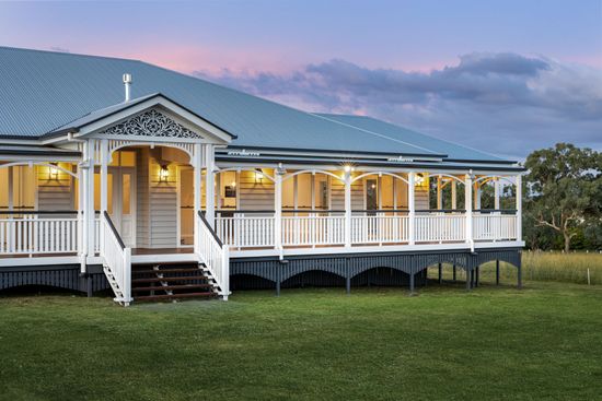 A white and gray Queenslander home with a wrap-around veranda on a grassy lawn at dusk.