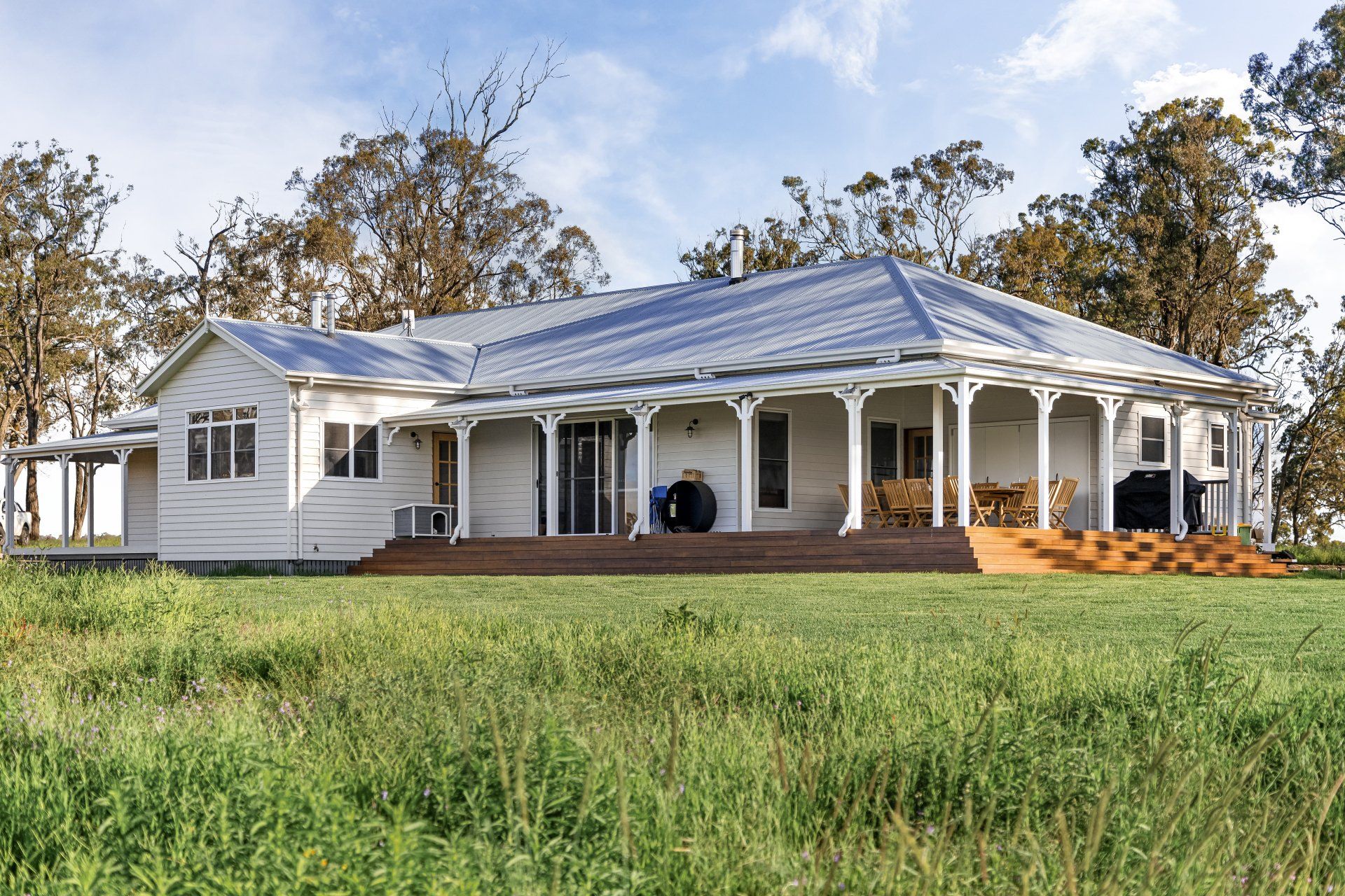 White farmhouse with wrap-around porch, on a grassy hill, under a bright sky.