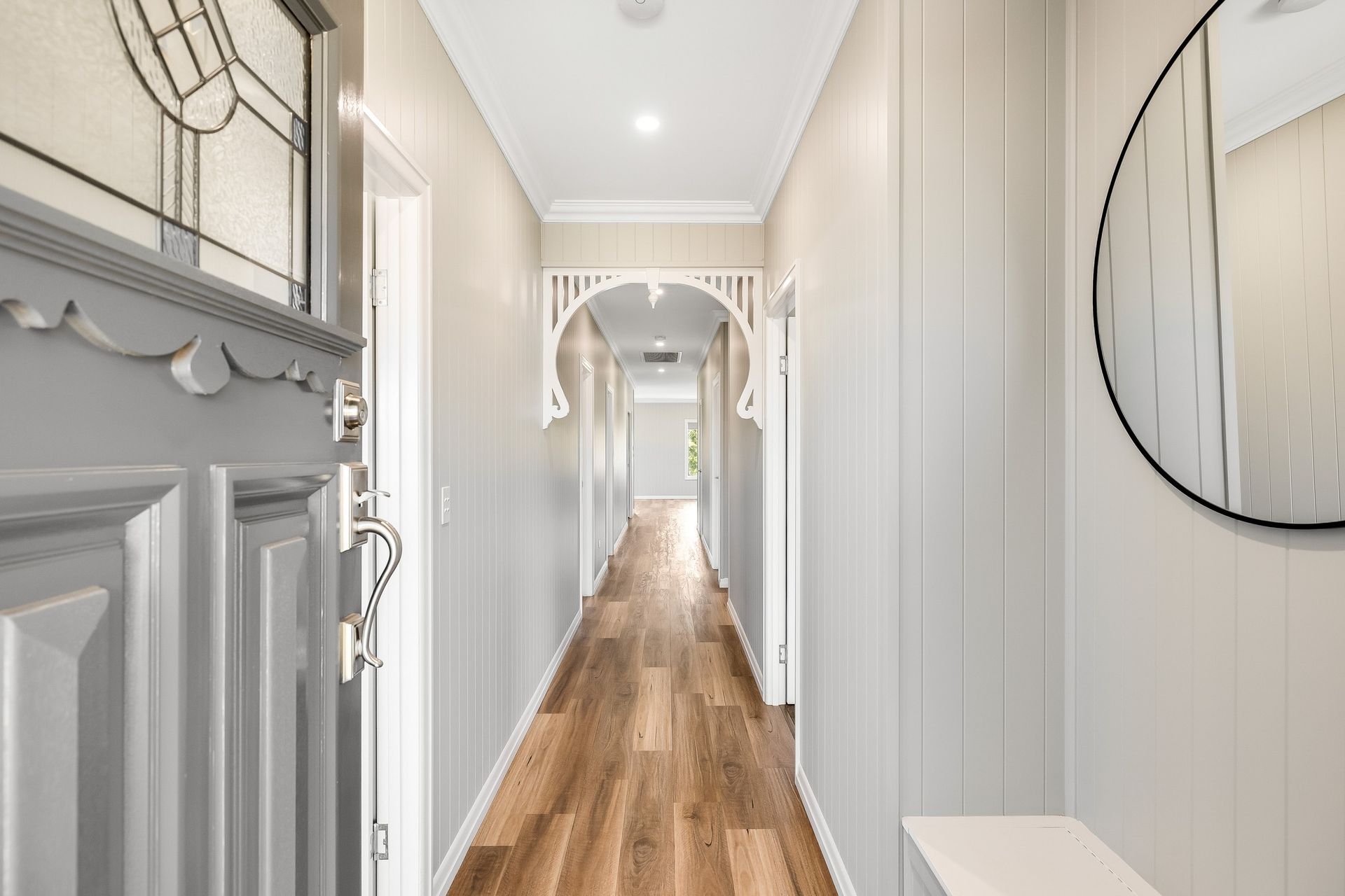 Long hallway with light wood floors, gray walls, white trim, and decorative archways.