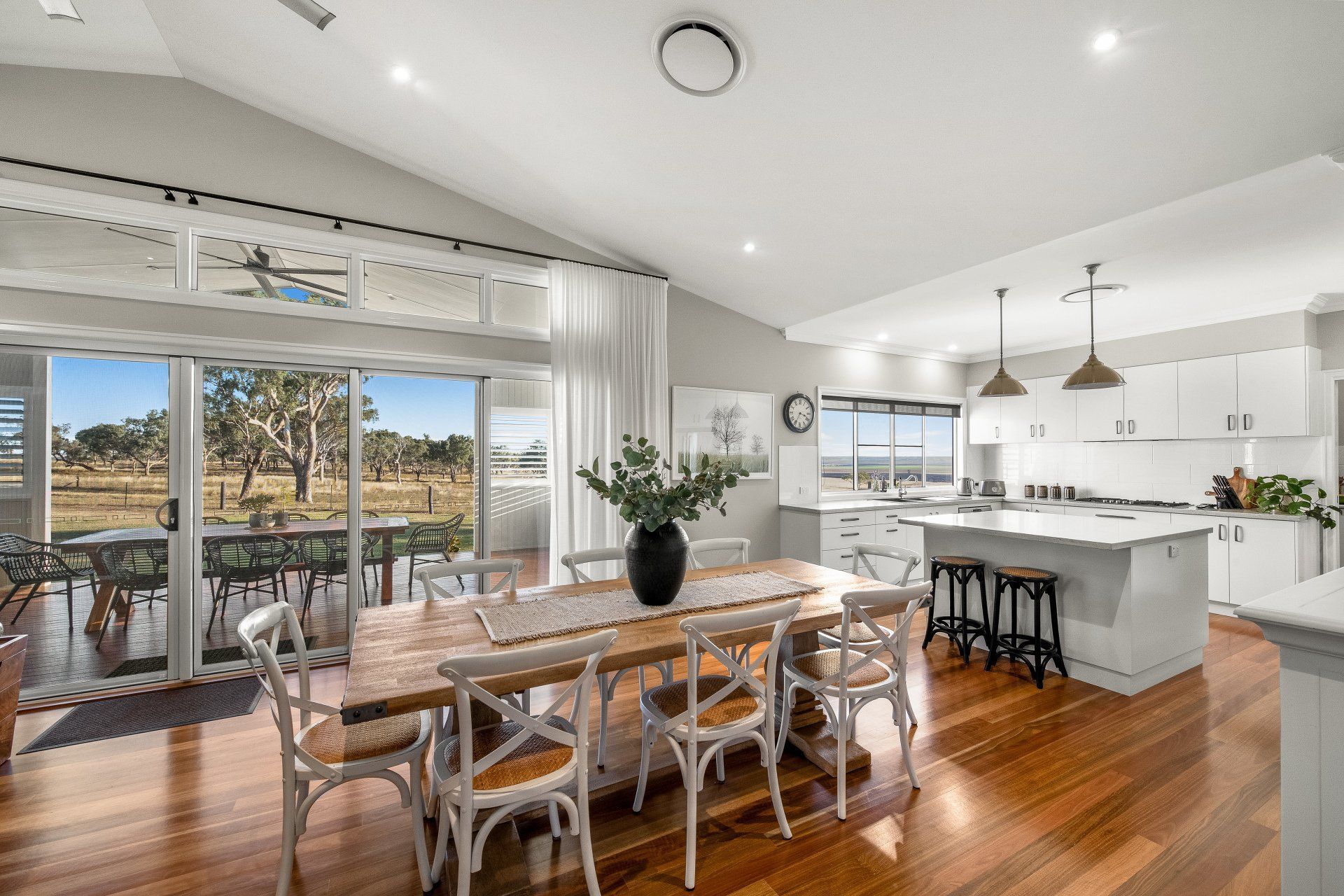 Open-concept kitchen and dining area with hardwood floors, white cabinets, and a long wooden table.
