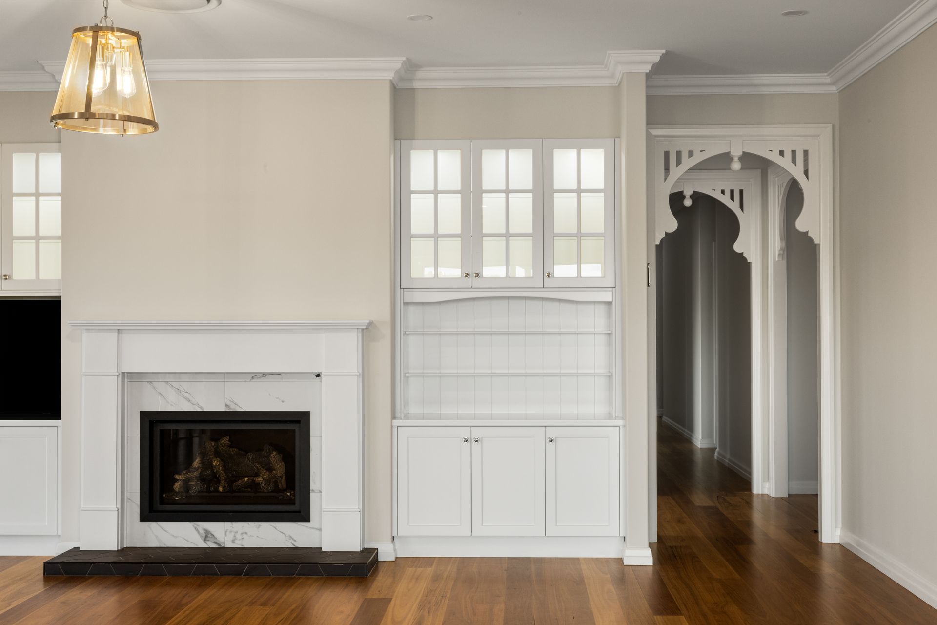 Living room with fireplace, built-in cabinets, and arched doorway, all painted white with wood floors.