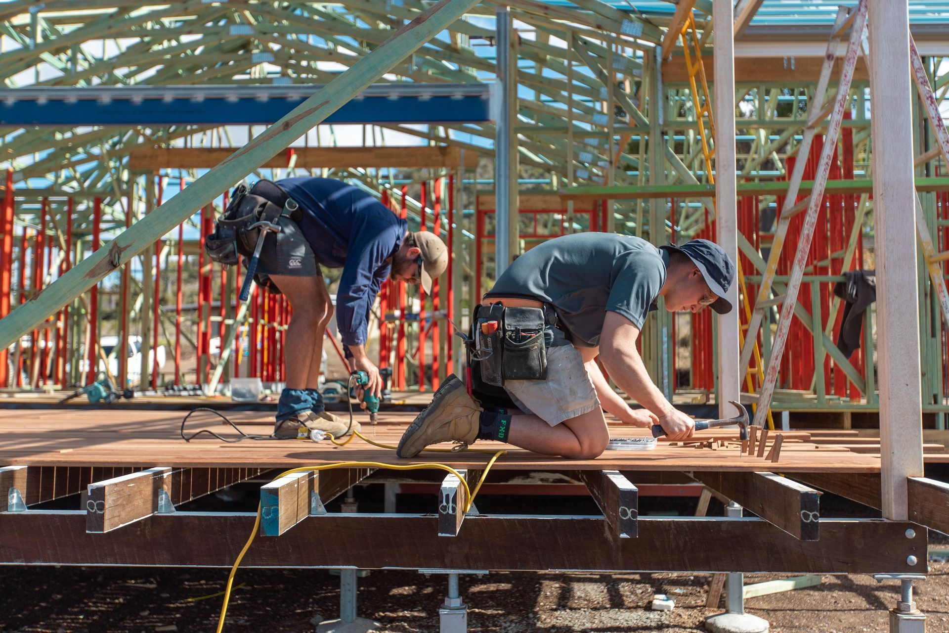 Two construction workers installing decking on a house frame.