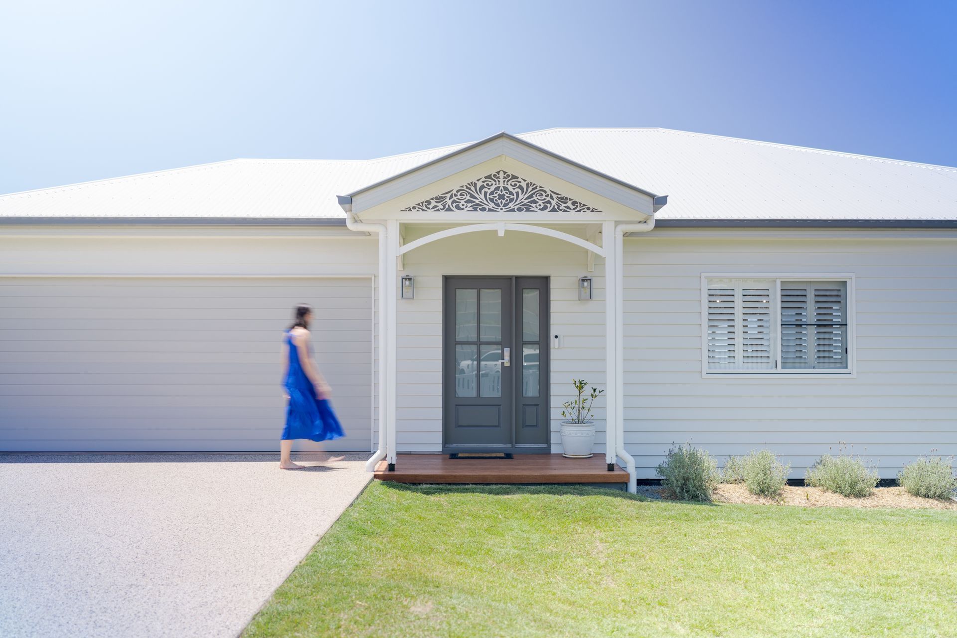 Woman in blue dress walks toward a white house with dark gray front doors.