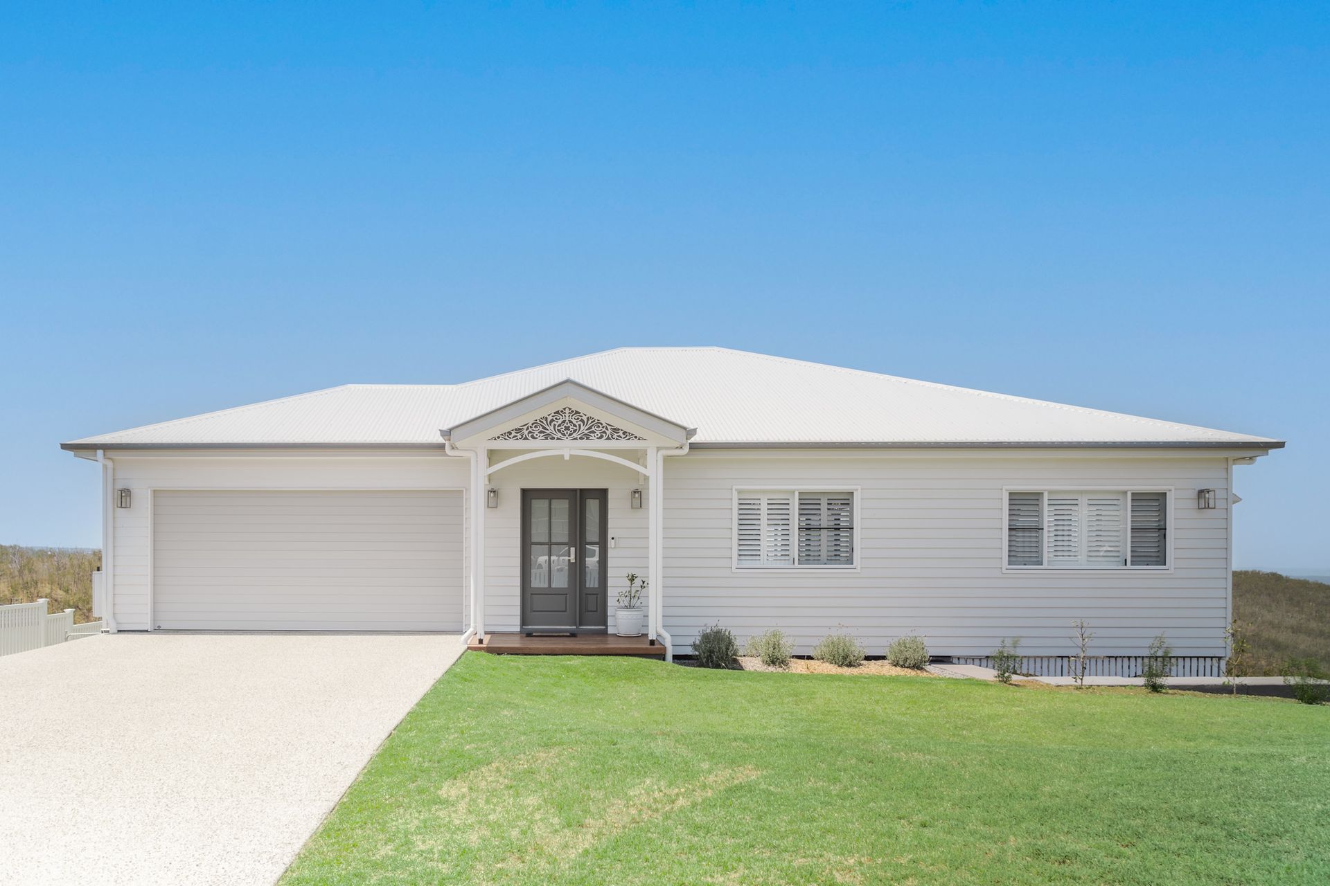 White house with a garage, front door, and green lawn against a blue sky.