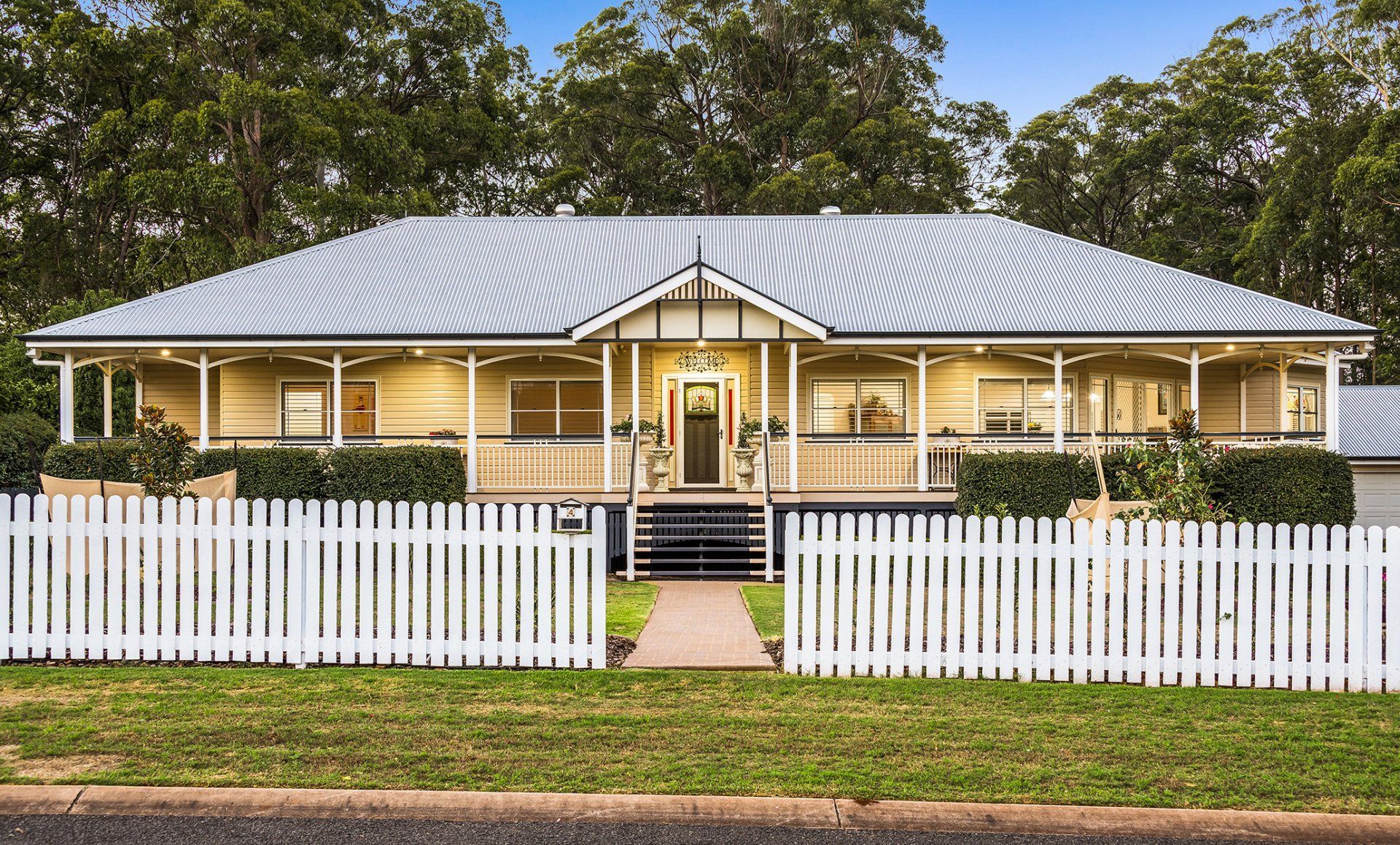 A light yellow bungalow with a white picket fence and a gray roof.