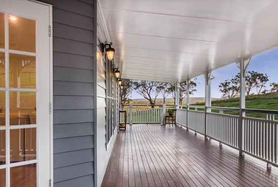 A covered wooden porch with a gray house and a scenic countryside view.