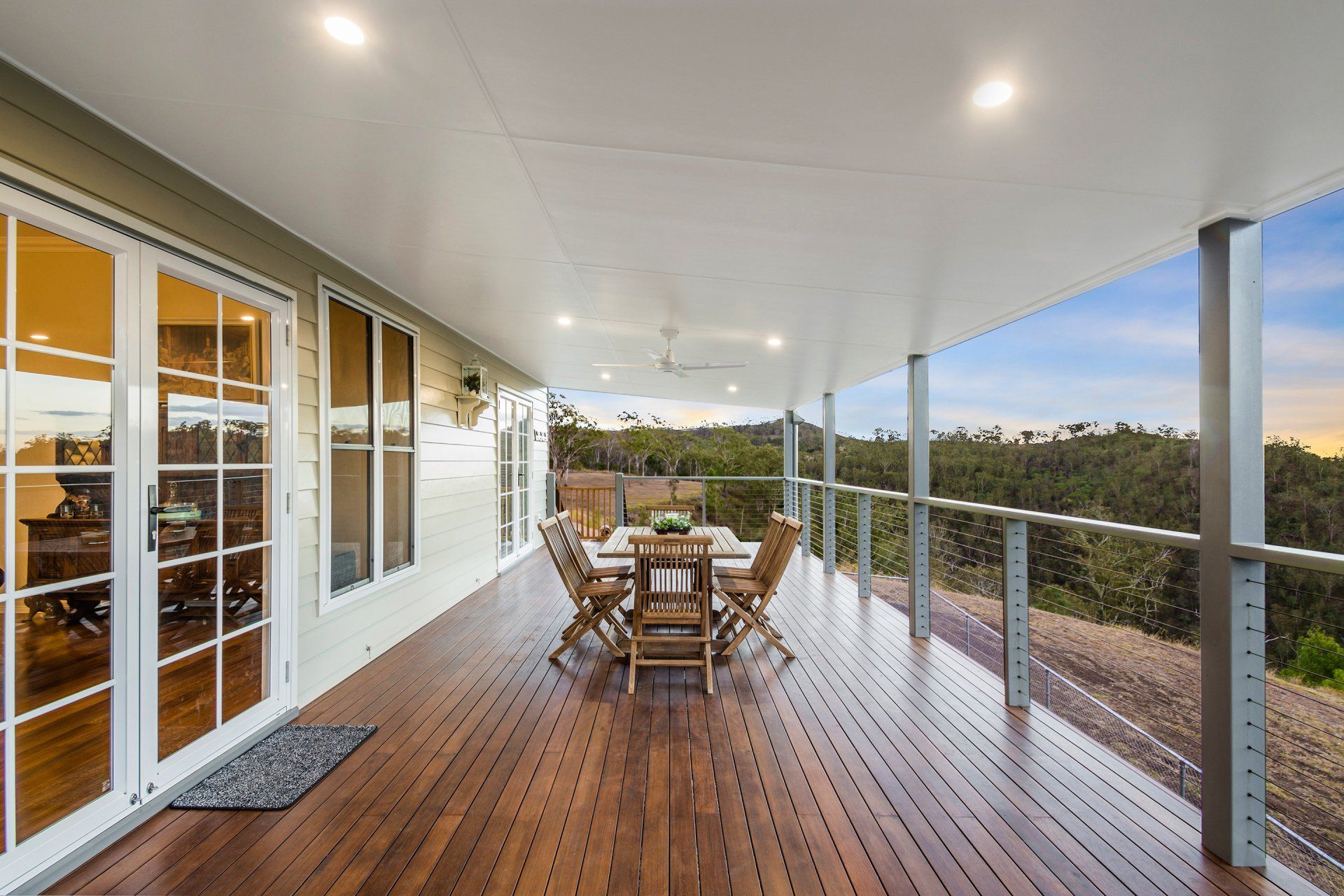Deck with dining table and chairs, overlooking a green landscape under a white ceiling.