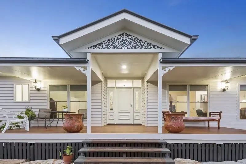 White country-style home with porch, steps, and decorative trim, set against a twilight sky.