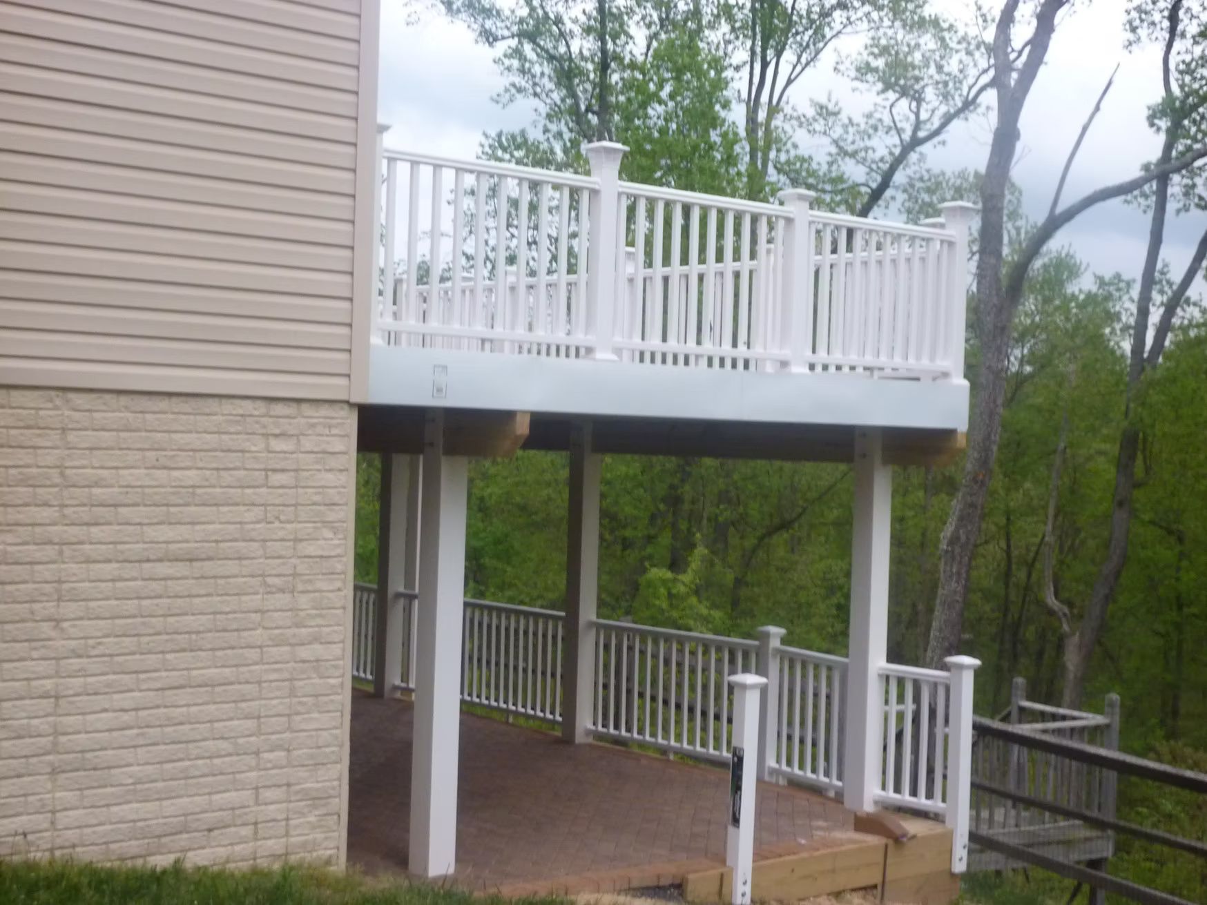 White-railed deck and covered patio beside a beige house, overlooking trees and a fenced yard