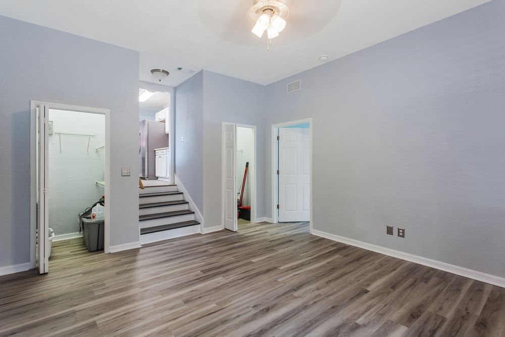 Empty light-blue room with wood flooring, staircase, and open doors to a bathroom and hallway.
