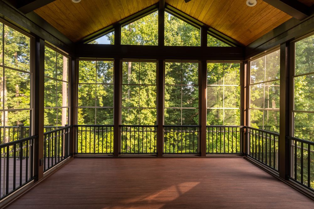 Empty screened porch with wood ceiling, dark railings, and large windows overlooking trees